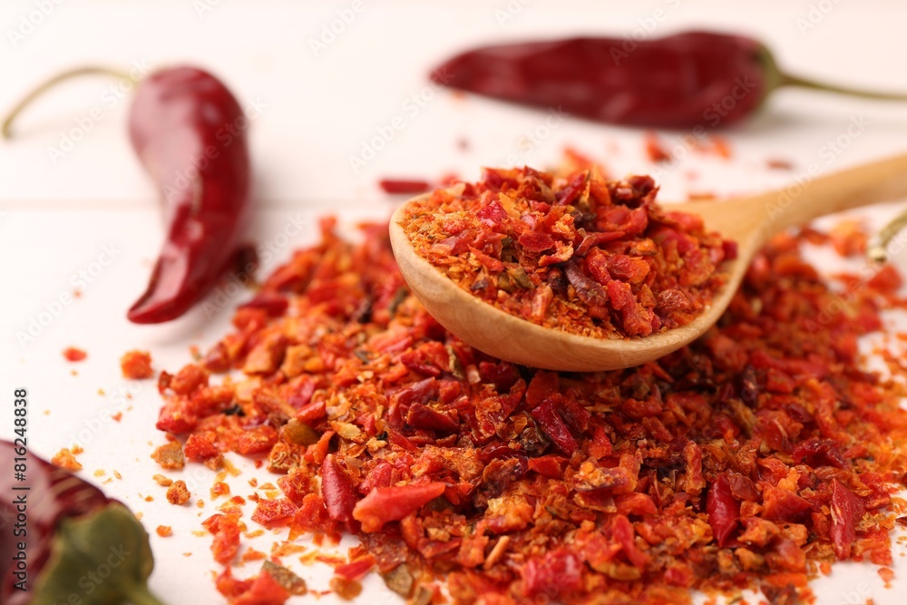 Chili pepper flakes and pods on white wooden table, closeup