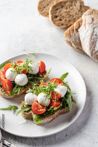 Sandwiches with tomatoes, mozzarella balls, arugula on white plate light textured background. Italian bruschetta set, antipasti