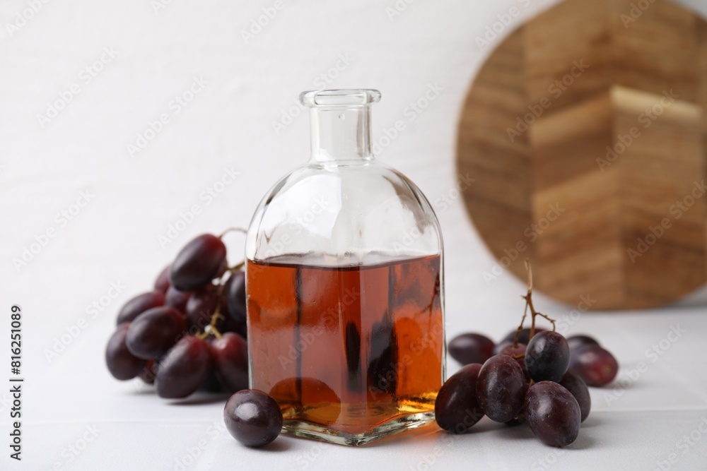 Wine vinegar in glass bottle and grapes on white table Wine vinegar in glass bottle and grapes on white table