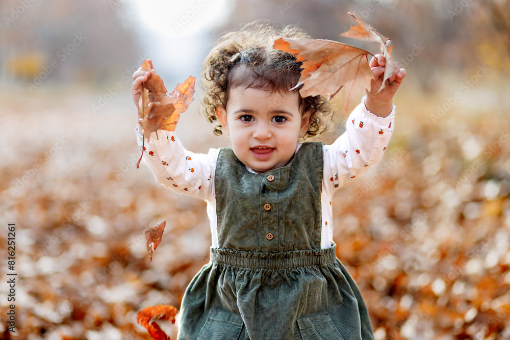 The joy of autumn. Playful little girl standing with leaves, amidst the season s painted leaves