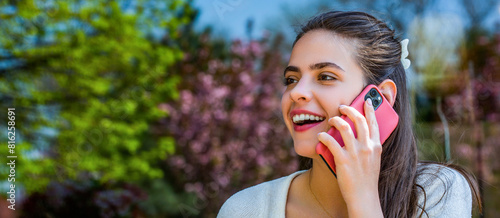 Young happy laughing woman talking on mobile phone isolated outdoors background. Cheerful woman is talking over the phone. Smiling girl talks on cellular telephone outdoors