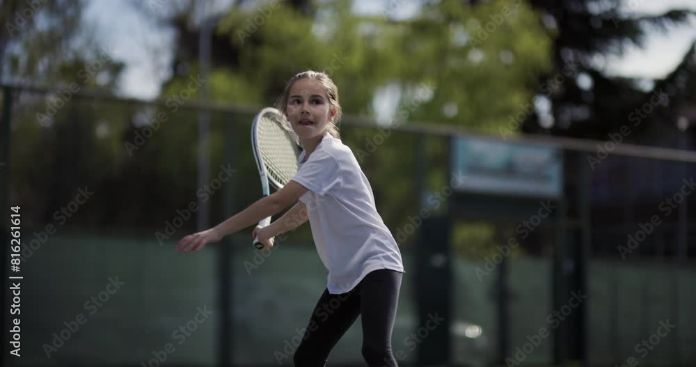 A focused young girl practices tennis on an outdoor court, displaying concentration and athletic skills. A focused young girl practices tennis on an outdoor court, displaying concentration and athletic skills.