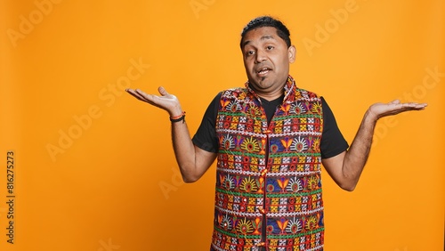 Indian man shrugging shoulders, unable to provide answer, having detached apathy facial expression. Apathetic person doing hand gesturing showing lack of knowledge, studio background, camera B