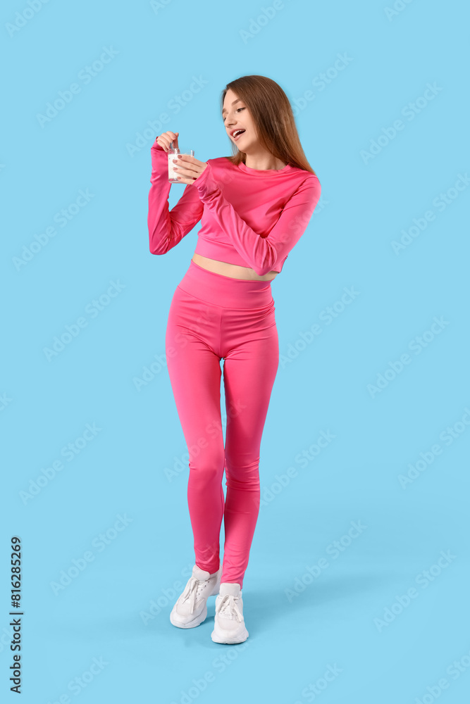 Sporty young woman with tasty yoghurt on blue background