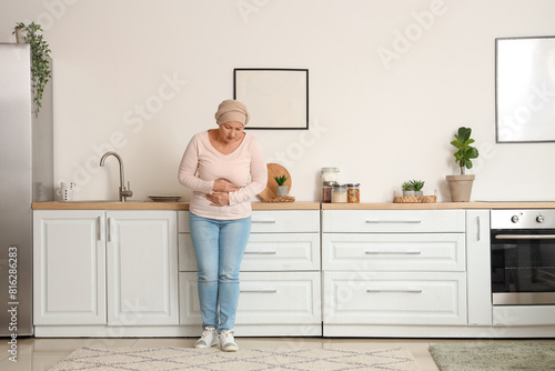Mature woman after chemotherapy suffering from pain in kitchen. Stomach cancer concept