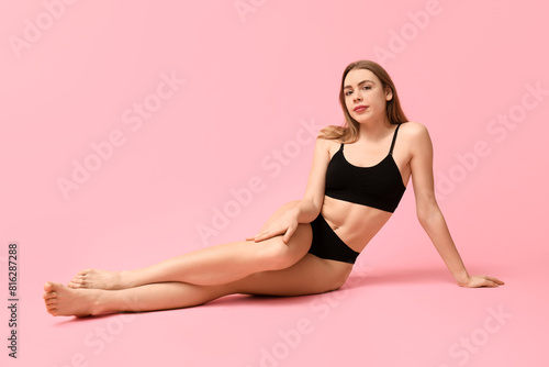 Sexy young woman in black cotton underwear sitting against pink background