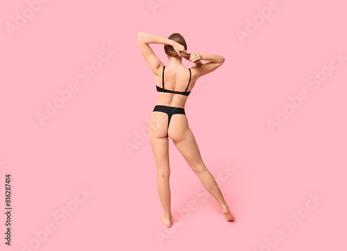 Pretty young woman in black underwear on pink background, back view