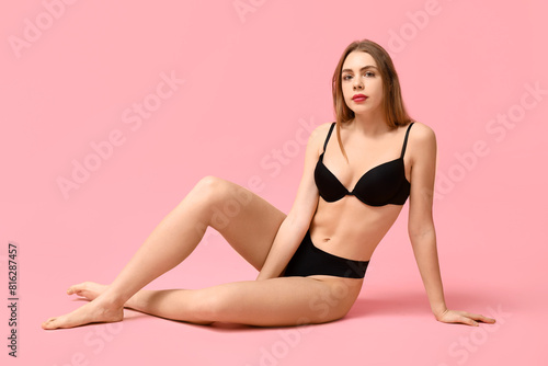 Pretty young woman in black underwear sitting against pink background