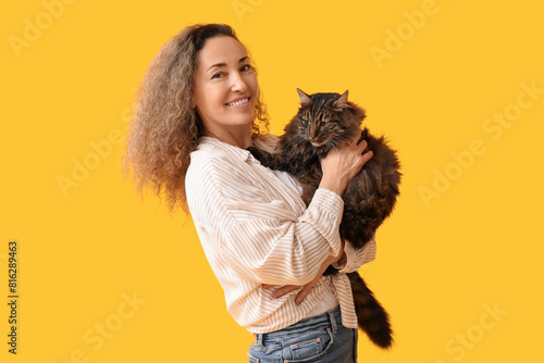 Happy mature woman with cute cat on yellow background