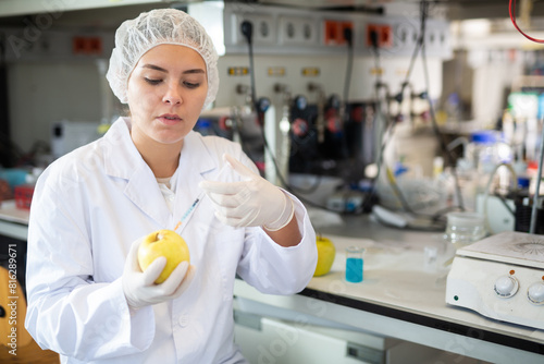 Professional female geneticist working in laboratory, injecting additives into apple during experiments with genetically modified apple