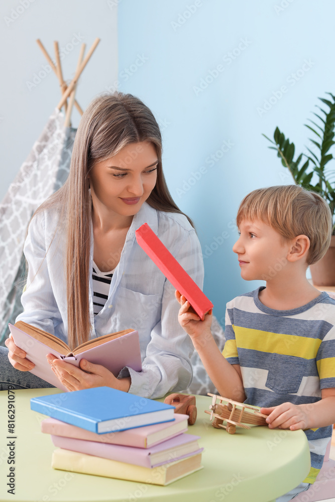 Fototapeta premium Mother and her son with different books sitting at table in children's room