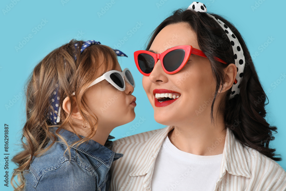 Beautiful pin-up woman and her daughter in sunglasses on blue background