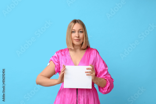 Woman with glucose sensor for measuring blood sugar level and blank paper on blue background. Diabetes concept