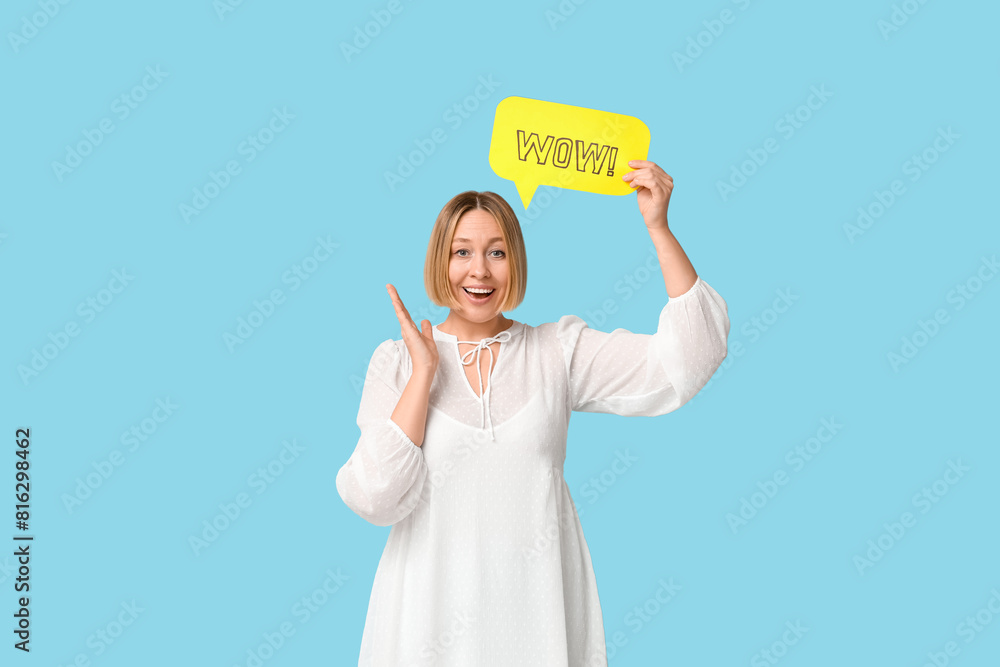 Surprised adult woman holding speech bubble with word WOW on blue background Surprised adult woman holding speech bubble with word WOW on blue background