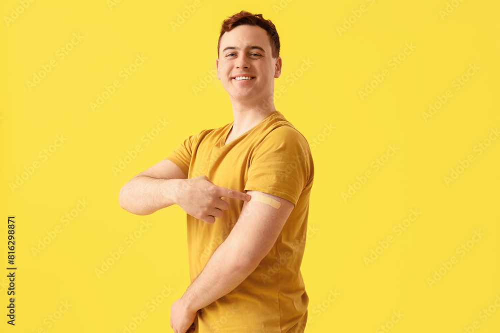 Happy young man with applied medical patch on yellow background. Vaccination concept Happy young man with applied medical patch on yellow background. Vaccination concept