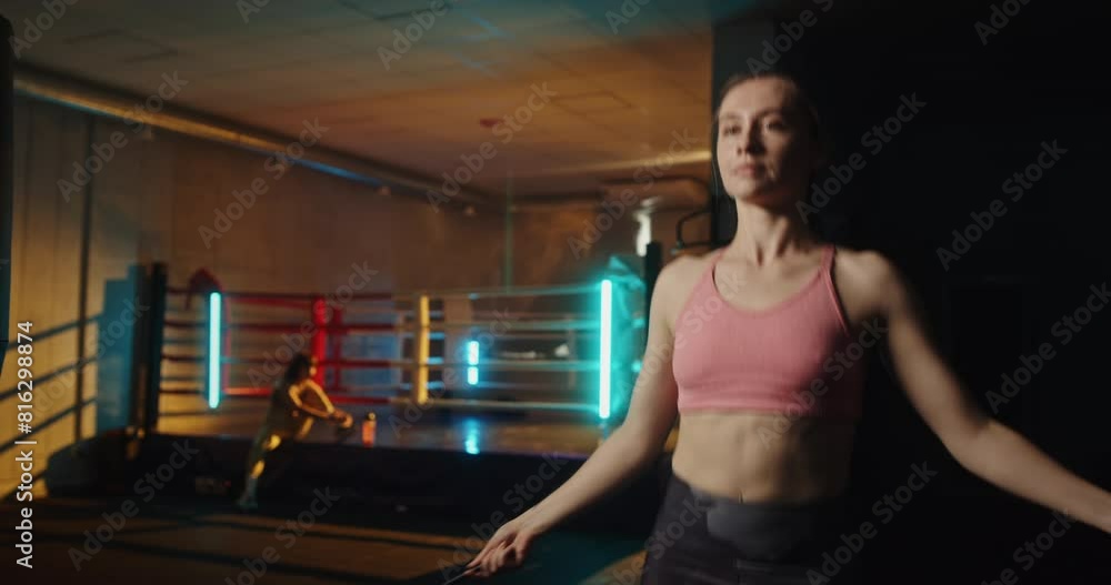 Athletic woman jumping rope in a boxing gym with colored lights while another woman warms up in the background, highlighting fitness routines, training, and active lifestyle in a modern indoor workout Athletic woman jumping rope in a boxing gym with colored lights while another woman warms up in the background, highlighting fitness routines, training, and active lifestyle in a modern indoor workout
