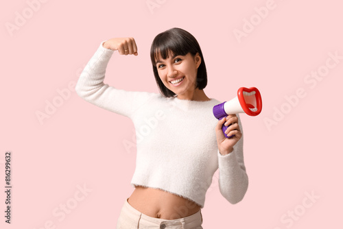 Young woman with megaphone showing muscles on pink background