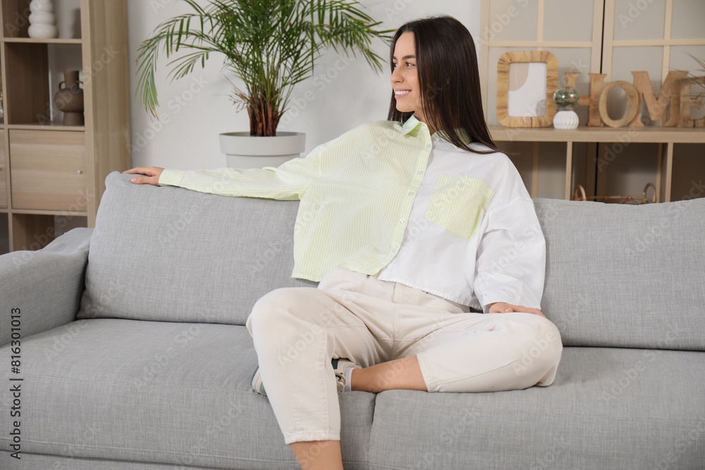 Pretty young woman sitting on grey sofa in living room Pretty young woman sitting on grey sofa in living room