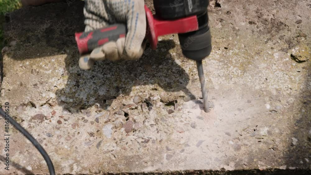 Close up of contractor drilling holes in concrete with an SDS hammer drill power tool to break up large concrete block into smaller pieces. Close up of contractor drilling holes in concrete with an SDS hammer drill power tool to break up large concrete block into smaller pieces.