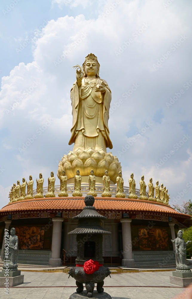 BANGKOK, THAILAND - May 16, 2024: A large golden statue of the Goddess Kuan Yin Set tall and elegant and small statues of the Goddess Kuan Yin decorated around with blue sky background.