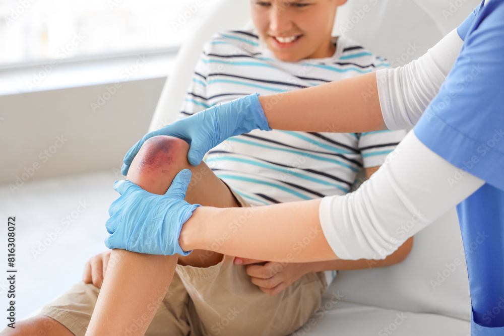 Fototapeta premium Little boy with bruised knee visiting doctor in clinic, closeup