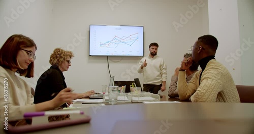 Multigenerational business team reviews growth statistics and analyzes chart data on a screen during a strategic planning session.