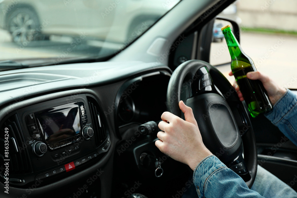 Man with bottle of beer driving car, closeup. Don't drink and drive concept Man with bottle of beer driving car, closeup. Don't drink and drive concept