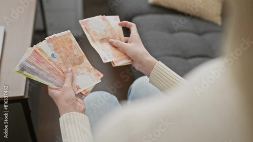 A woman counts philippine pesos in her cozy living room, indicating finance, budgeting, or travel preparation. photo