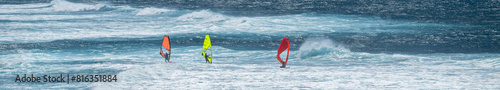 Photography Three colorful windsurfers, red, orange, and yellow, racing in the wind on the P
