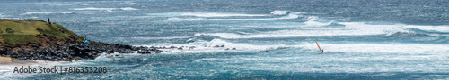 Man on a wind surfer with red sail riding the wind on the Pacific Ocean off the coast of Maui at Hookipa Beach, Hawaii 