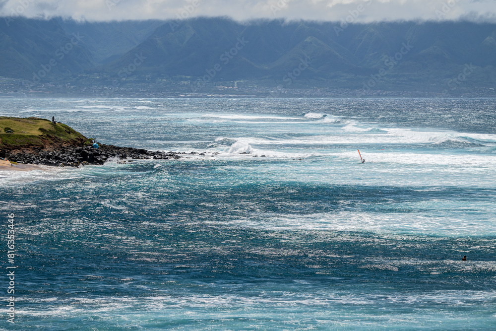 Man on a wind surfer with red sail riding the wind on the Pacific Ocean off the coast of Maui at Hookipa Beach, Hawaii
