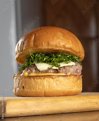 A big hamburger with brioche bread, meat, cheese, mustard sauce and crispy cabbage on a wooden table