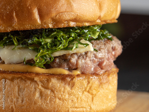 A closeup of a big hamburger with brioche bread, meat, cheese, mustard sauce, and crispy cabbage on a wooden table