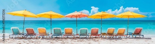 Row of colorful beach chairs and umbrellas are set up on a beach. The umbrellas are yellow and orange, and the chairs are in various colors.