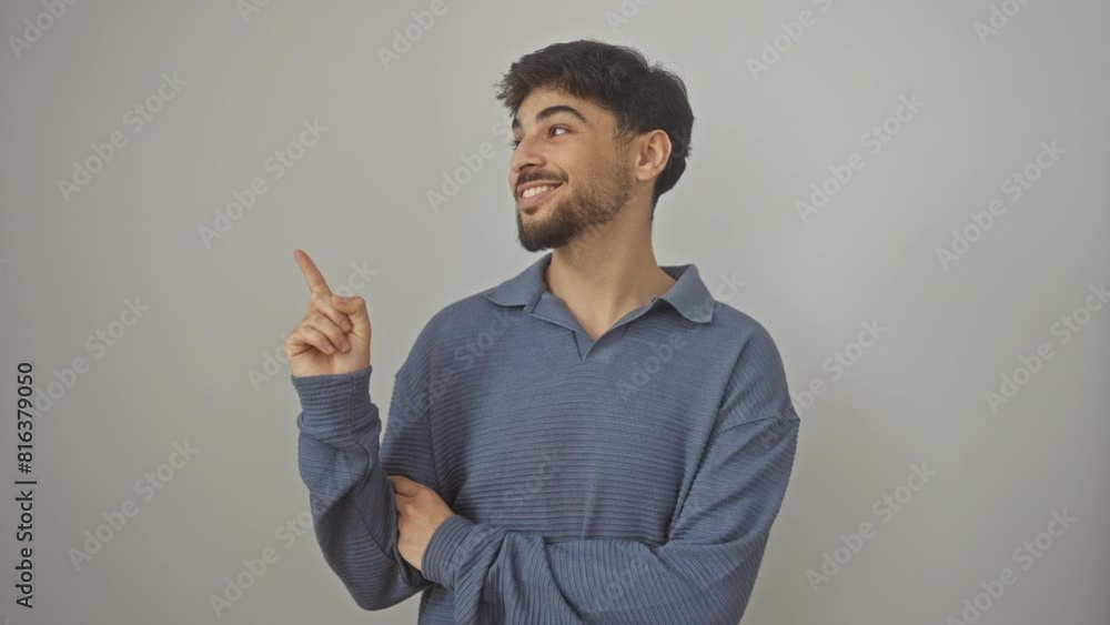 Cheerful young arab man, standing alone on an isolated white background, smiling joyfully while pointing to the side with his hand and finger Cheerful young arab man, standing alone on an isolated white background, smiling joyfully while pointing to the side with his hand and finger
