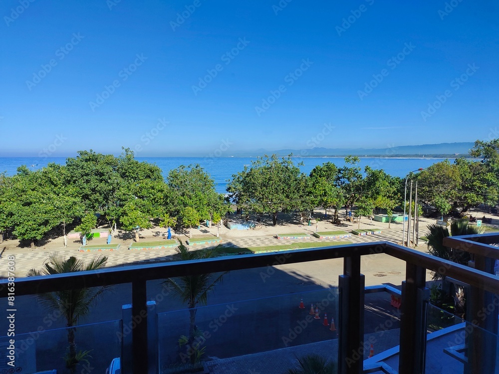 Sunny Beachfront View from Hotel Balcony with Bright Sunlight and Clear Blue Sky