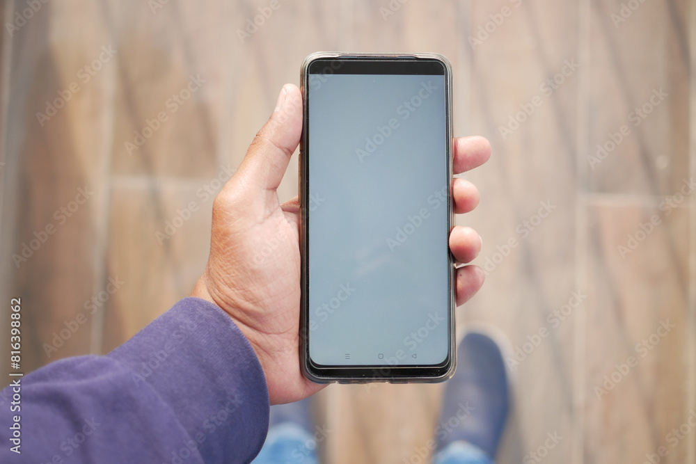 POV shot of holding smart phone with white screen against wooden floor POV shot of holding smart phone with white screen against wooden floor