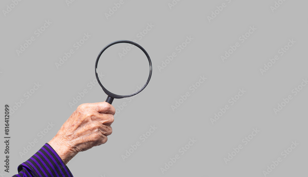 Close-up of an old woman's hand holding a magnifying glass against a gray background. Close-up of an old woman's hand holding a magnifying glass against a gray background.