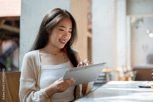 A beautiful Asian woman is using her digital tablet while sitting at an outdoor table of a cafe.