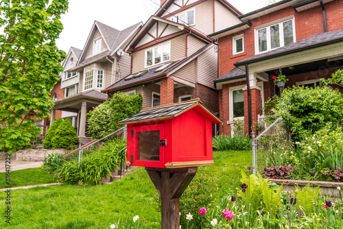 A free book exchange box, bright red, on a residential street shot in the toronto beaches neighbourhood in spring room for text 