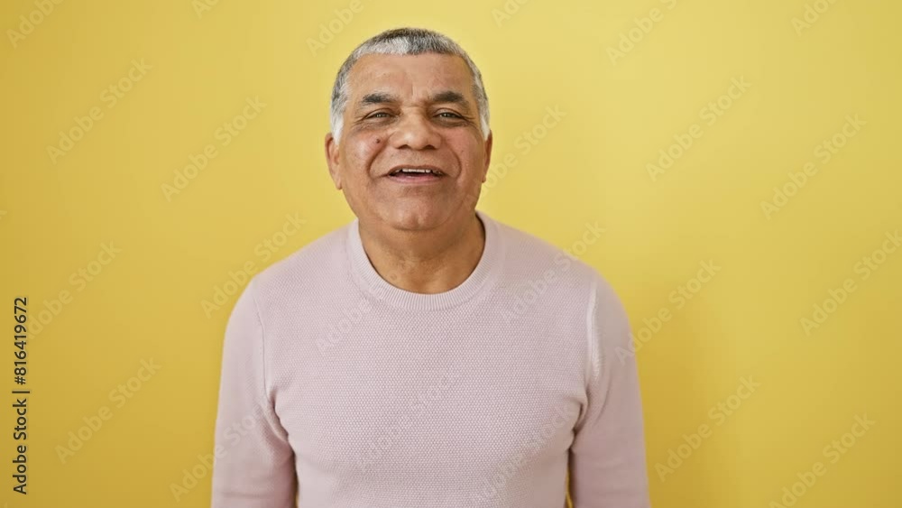 Cute grey-haired latin man in sweater blowing a kiss to camera. confident and sexy expression of love. standing against a yellow, isolated background Cute grey-haired latin man in sweater blowing a kiss to camera. confident and sexy expression of love. standing against a yellow, isolated background