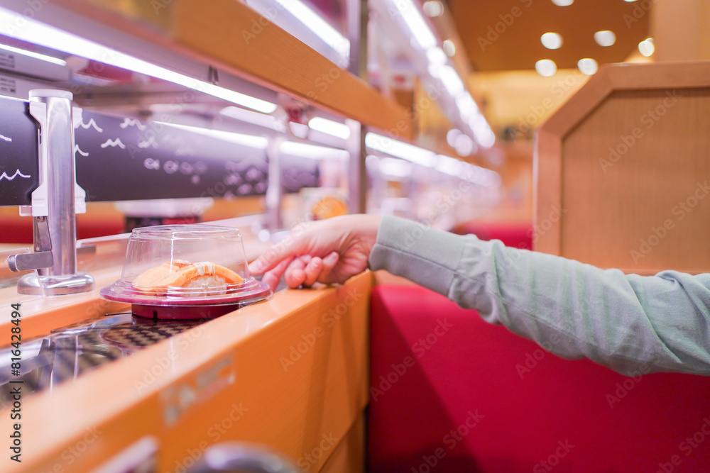Obraz premium Happy Asian woman eating Sushi at modern Japanese conveyor belt Sushi bar.