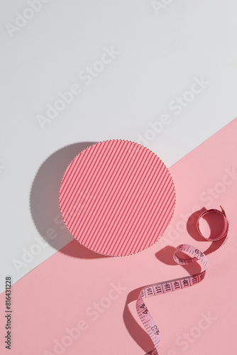 High angle shot photo at a pink blank podium with plaid pattern placed on white and pink background, decorated with a pink measuring tape. Space for displaying product of weight losing theme