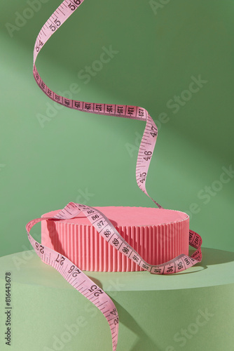 Minimalist photo with a blank pink pedestal isolated on green background, a pink measuring tube floating decorated. Blank space for displaying products that support weight loss, frontal shot