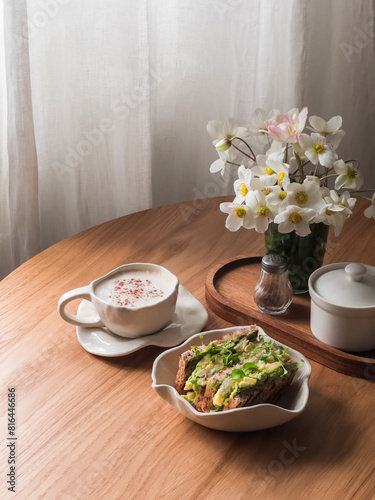 Delicious breakfast  - cappuccino and avocado, eggs, microgreens toast on a round wooden table, top view. Aesthetic food concept