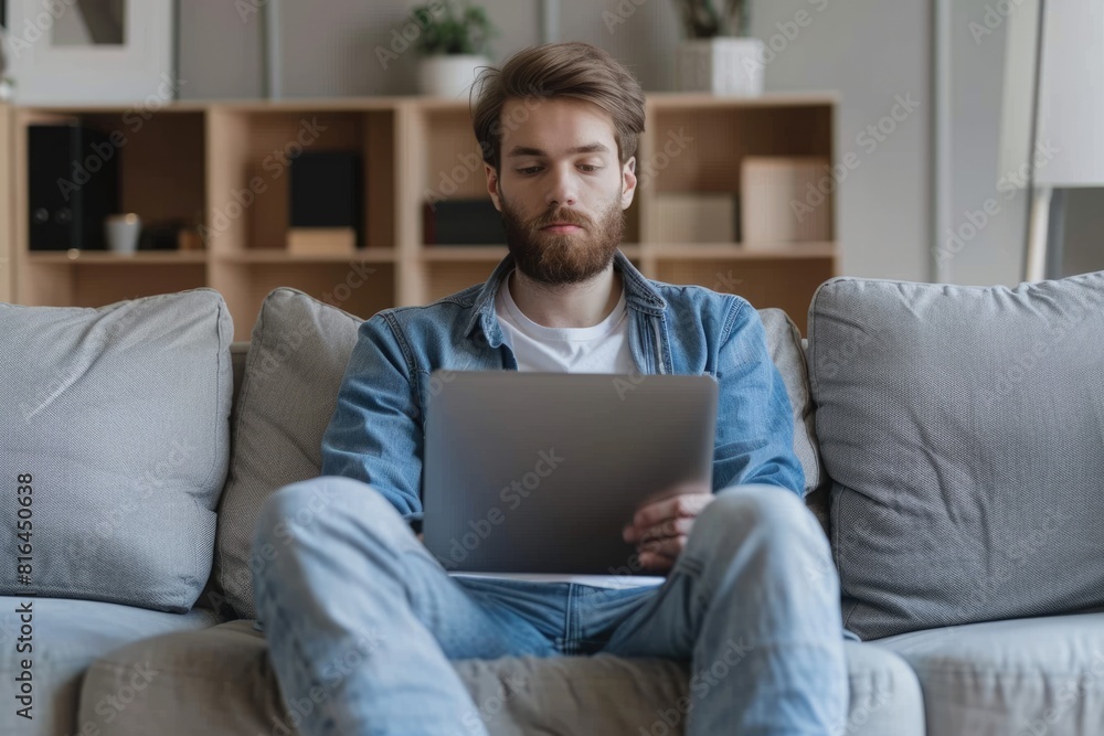 Man In Home. Concentrated Young Bearded Man Sitting on Couch and Using Laptop Computer at Home Man In Home. Concentrated Young Bearded Man Sitting on Couch and Using Laptop Computer at Home