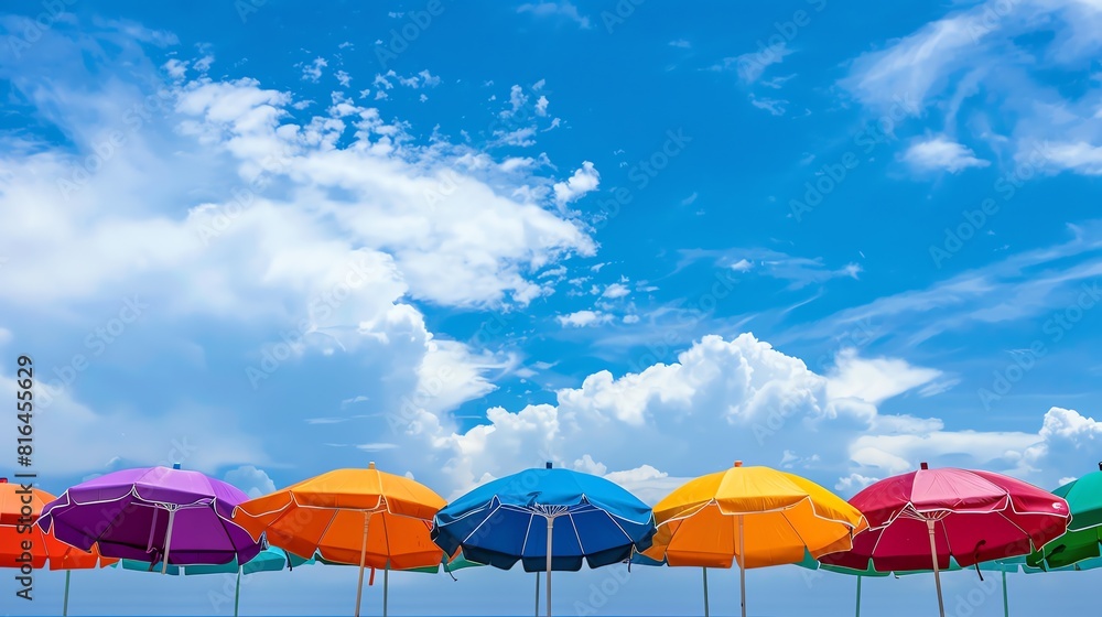 Canopy of colorful beach umbrellas against a vibrant blue sky and fluffy white clouds.