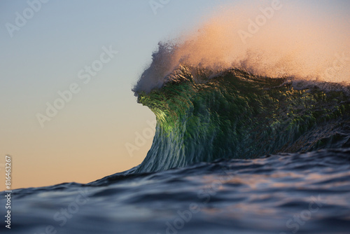 The crest of a vibrant heavy green ocean wave rising up to explode on a shallow reef