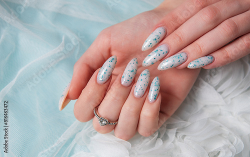Female hands with blue nail design on blue silk background.