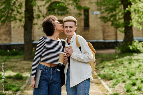 Two young women in stylish attire sharing a tender kiss amidst lush greenery in the park. © Bliss